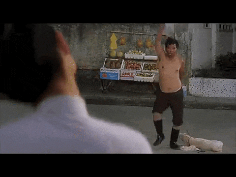 a man without a shirt is standing in front of a fruit stand on a street .