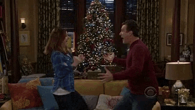 a man and a woman are dancing in a living room in front of a christmas tree .