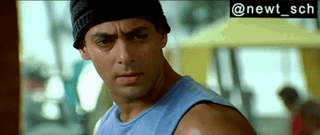 a close up of a man wearing a blue tank top and a beanie