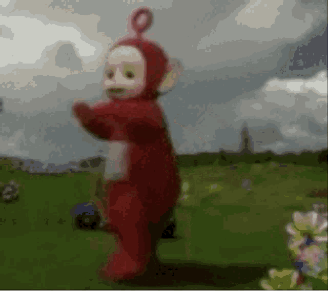 a teletubbies character is dancing in a field with flowers in the background .