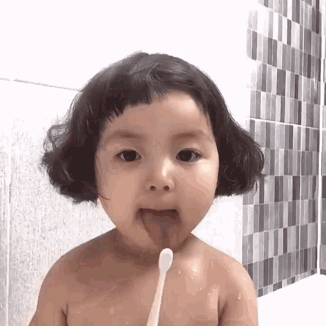 a baby girl is sticking her tongue out while brushing her teeth in the bathroom .