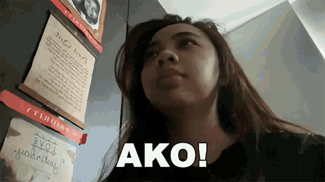 a woman stands in front of a wall with a sign that says " ako "