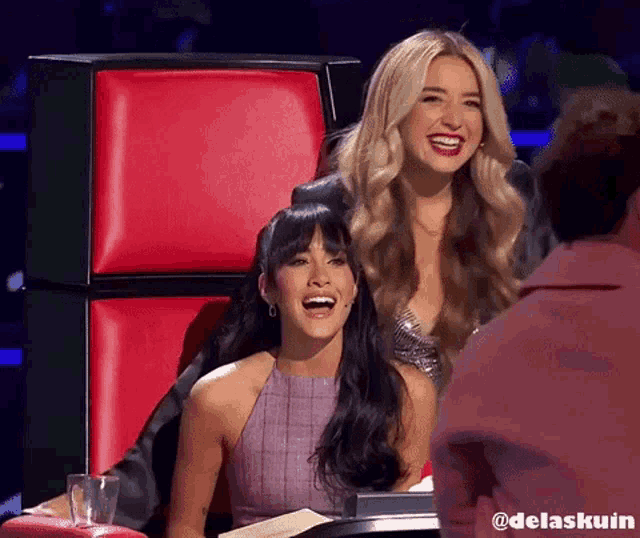 two women are sitting next to each other on a red chair and one of them has the word delaskuin on the bottom