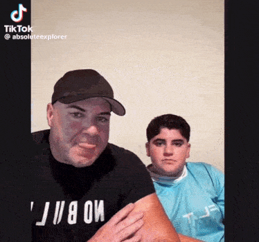 a man and a boy are posing for a picture and the boy is wearing a blue shirt that says t-j-f