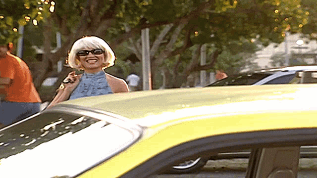 a woman wearing sunglasses is standing next to a yellow car and smiling