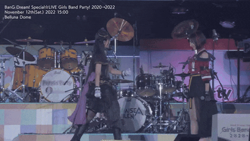 two girls are standing on a stage in front of a drum set that says aisea uilen