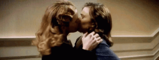 a man and a woman are kissing in front of a wall .