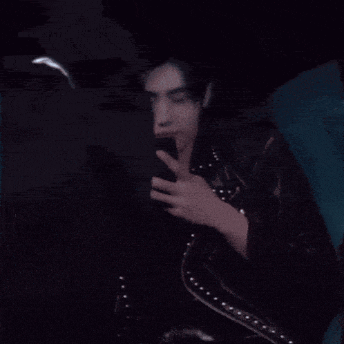 a woman in a black leather jacket is sitting on a blue couch with her hand on her chest
