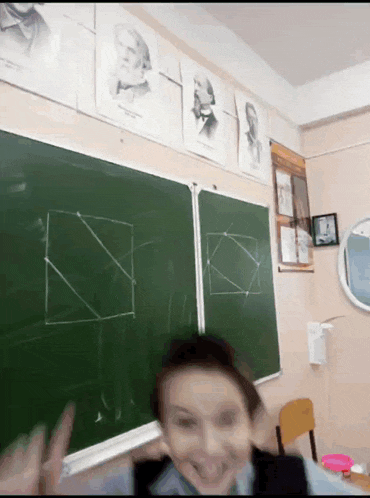 a boy stands in front of a chalkboard in a classroom