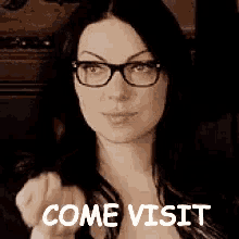 a woman wearing glasses is pointing at the camera and says come visit