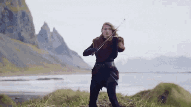 a woman is playing a violin in front of a mountain and a lake .