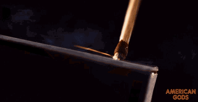 a close up of a burning stick with the words american gods on the bottom