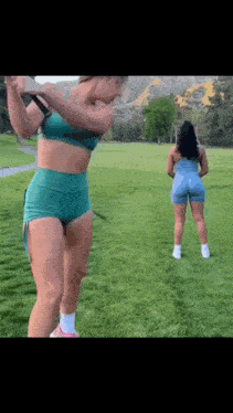 two women are standing on top of a lush green field holding a golf club .
