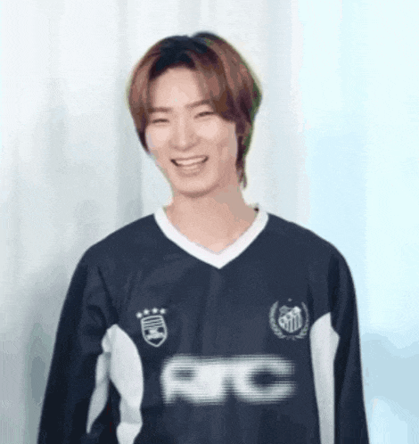 a young man wearing a soccer jersey is smiling and looking at the camera .