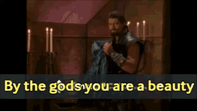 a man in a room with candles and the words " by the gods you are a beauty " above him