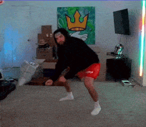 a man in a black hoodie and red shorts is dancing in front of a painting that says king