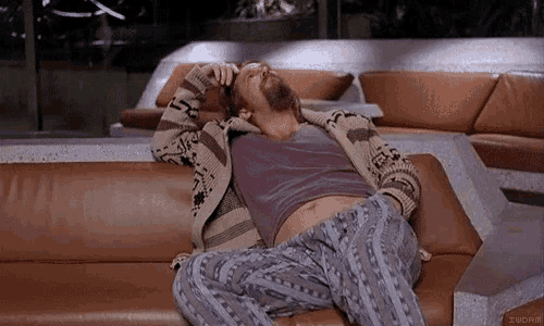a man is laying on a couch wearing pajamas and a sweater and talking on a cell phone .