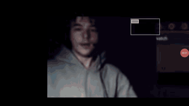 a man in a hoodie is sitting in front of a computer screen with a red circle that says stop on it .