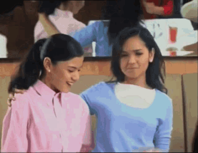 two women standing next to each other with one wearing a pink shirt and the other wearing a blue sweater