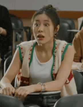 a woman is sitting in a classroom wearing a sweater vest and a white shirt