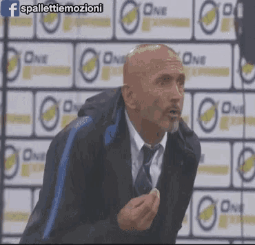 a bald man in a suit and tie stands in front of a wall that says one on it