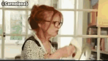 a woman with red hair wearing glasses is standing in front of a window with the hashtag carmelona5