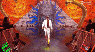 a man in a white suit is walking through a pyramid with a statue in the background