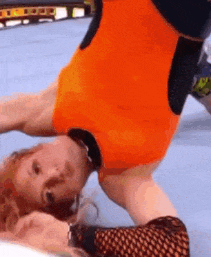a woman in an orange leotard is doing a handstand in a wrestling match .