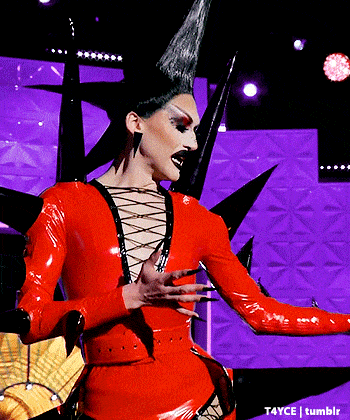 a drag queen is wearing a red latex outfit with spikes on her head .