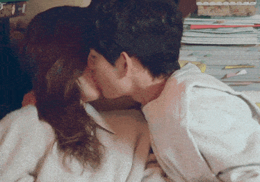 a man and woman are kissing in front of a stack of books