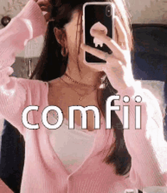 a woman in a pink sweater is taking a picture of herself in the mirror .