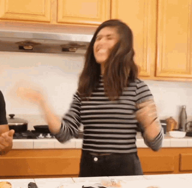a woman in a striped shirt is standing in a kitchen with her arms in the air