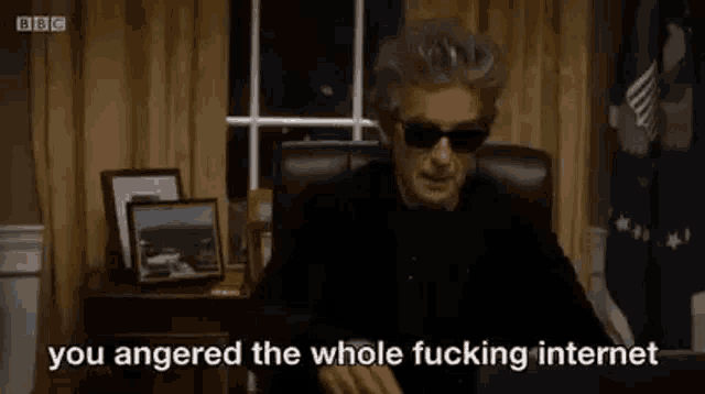a man wearing sunglasses is sitting at a desk with a laptop and says `` you angered the whole fucking internet '' .