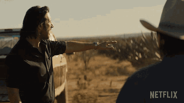a man in a cowboy hat is pointing at something while another man looks on