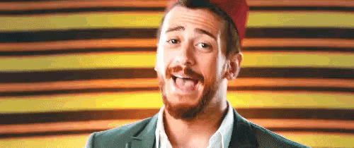 a man with a beard is wearing a red hat and a green suit .