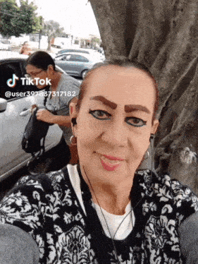 a woman with eyeliner on her eyebrows is taking a selfie with a car in the background