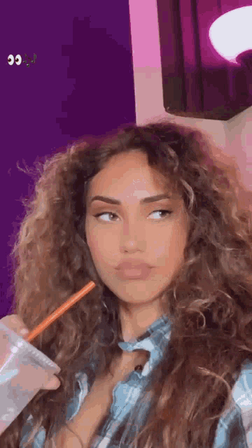 a woman with long curly hair is drinking a drink with a straw .