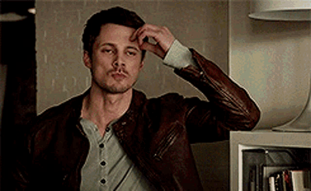 a man wearing a brown leather jacket is sitting in a room .