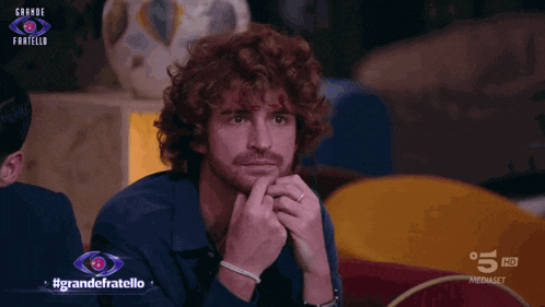 a man with curly hair and a ring on his finger is on a television screen that says grande fratello
