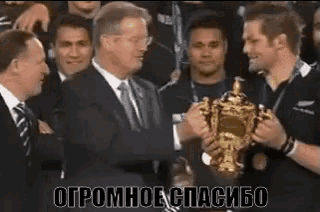 a man in a suit and tie is shaking hands with another man holding a trophy .