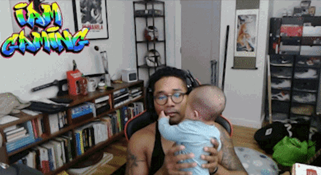 a man is holding a baby in front of a wall with graffiti that says ' t & m gaming ' on it