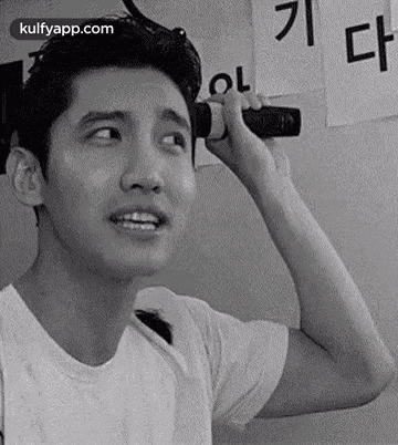 a black and white photo of a man holding a microphone to his ear and making a funny face .