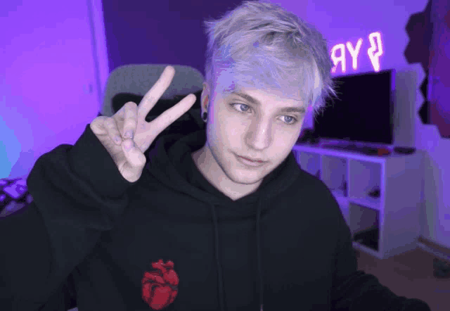 a young man giving the peace sign in front of a purple sign that says ay