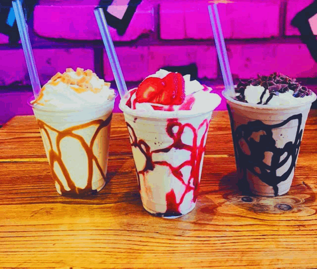 three milkshakes on a wooden table with straws