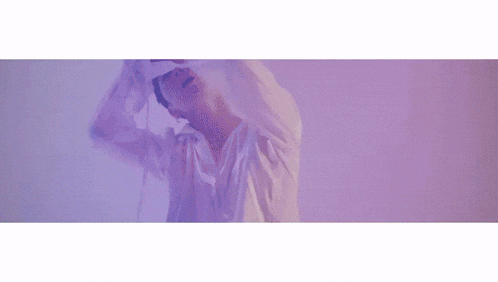 a man in a white shirt is standing in front of a pink wall holding a towel over his head .