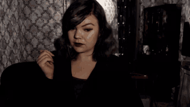 a woman in a dark room with a patterned wall behind her