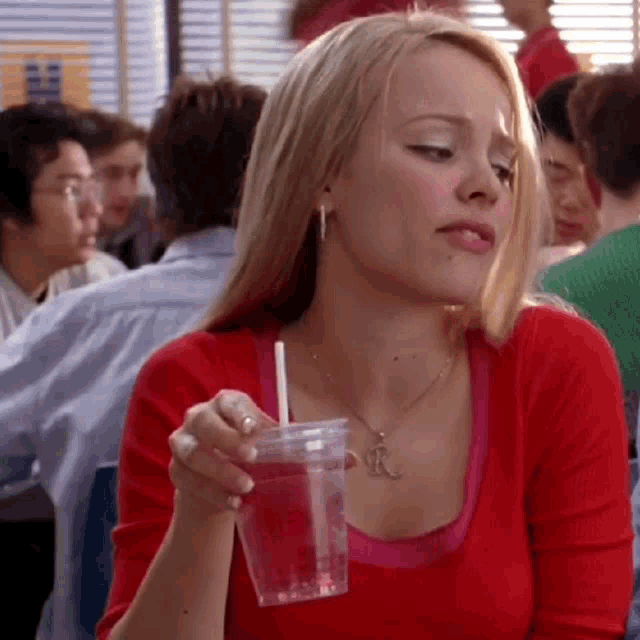 a woman in a red shirt is drinking from a clear cup with a straw