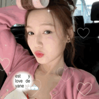 a woman in a pink cardigan is holding a roller in her hair while taking a selfie