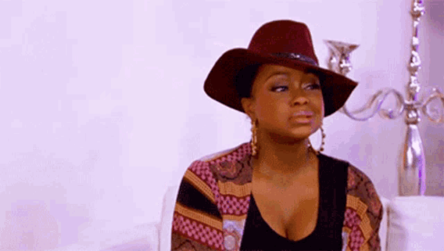 a woman wearing a cowboy hat and a cardigan is sitting on a couch .