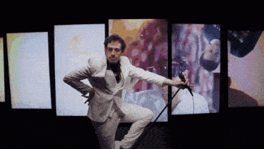 a man in a white suit is holding a microphone in front of a wall of pictures